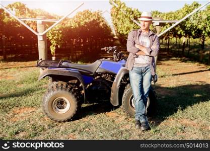 Man standing next to truck in vineyard. Man wearing hat standing next to truck in vineyard