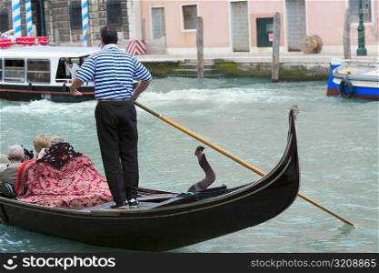 Man standing on a gondola in a canal, Grand Canal, Venice, Italy