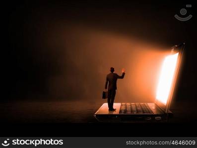 Man standing on big laptop. Rear view of businessman with suitcase standing on keyboard of big laptop