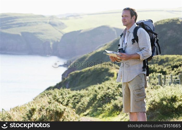Man standing on cliffside path holding map