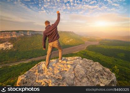 Man standing on top of a cliff with arm raised