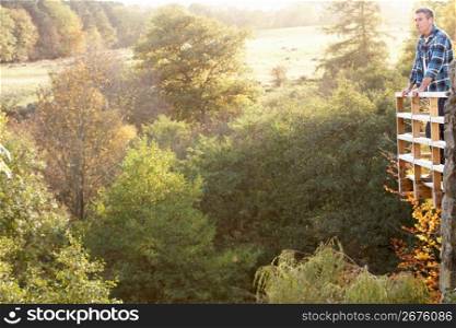 Man Standing On Wooden Balcony Overlooking Autumn Woodland