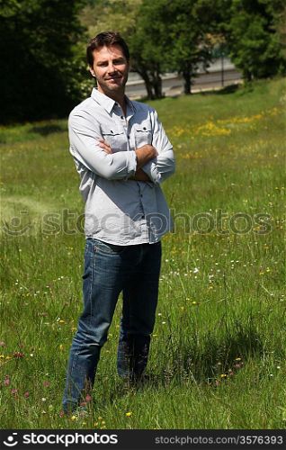 Man standing with arms crossed in a park