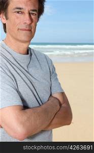 Man standing with his arms crossed on a sandy beach