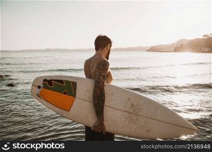 man standing with surfboard beach