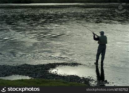 Man stands fishing on riverbank, Scotland