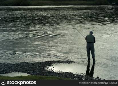 Man stands fishing on riverbank, Scotland