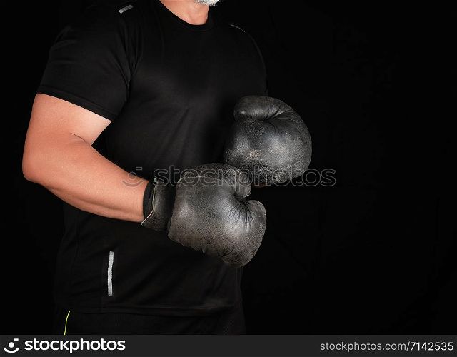 man stands in a boxing rack, wearing very old vintage black boxing gloves on his hands, dark background