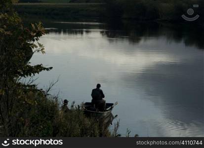 Man stands in rowing boat with still water, Scotland
