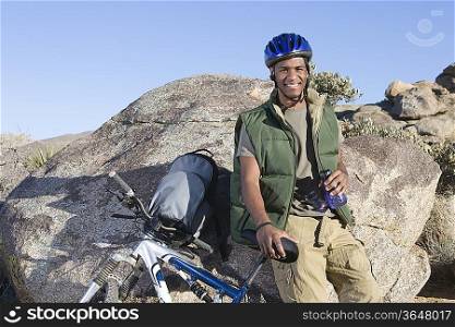Man stands leaning against rock with mountain bike