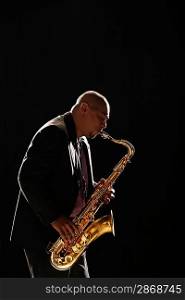 Man stands playing saxophone against black background