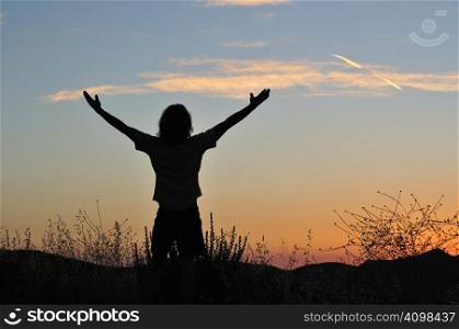 Man stands triumphant at sunset among the silhouettes of tall grasses.