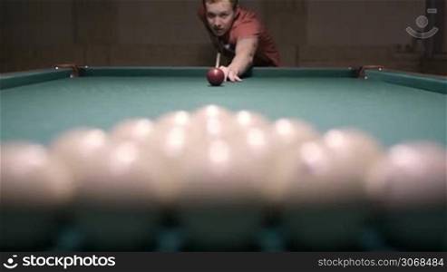 Man starting billiard game and breaking ball triangle. At first man in focus, then balls.