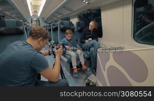 Man stocker shooting footage of a mother with son traveling by express train and passing time with pad and cellphone