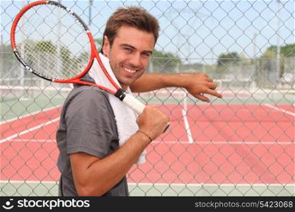 Man stood in front of tennis court holding racket over shoulder