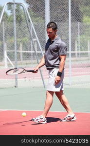 Man stood on outdoor tennis court bouncing ball with racket