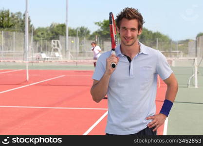 Man stood on outdoor tennis court holding racket over shoulder