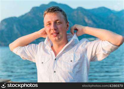 man straightens his shirt collar near the sea