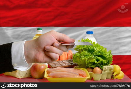 man stretching out credit card to buy food in front of complete wavy national flag of austria