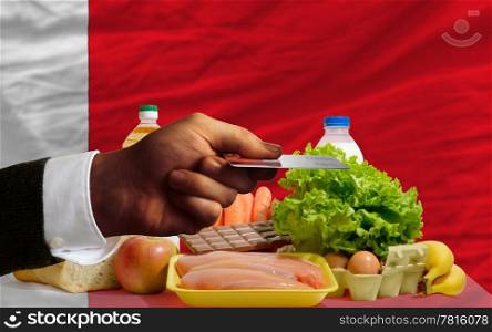 man stretching out credit card to buy food in front of complete wavy national flag of bahrain