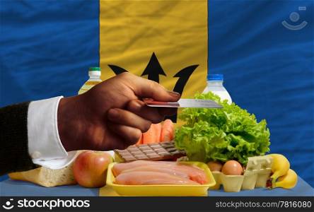 man stretching out credit card to buy food in front of complete wavy national flag of barbados