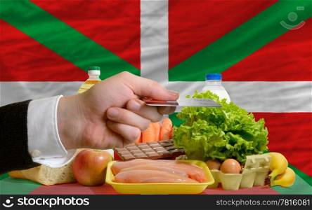 man stretching out credit card to buy food in front of complete wavy national flag of basque