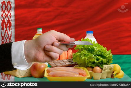 man stretching out credit card to buy food in front of complete wavy national flag of belarus