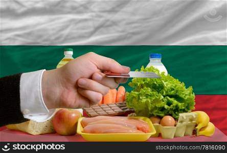 man stretching out credit card to buy food in front of complete wavy national flag of bulgaria