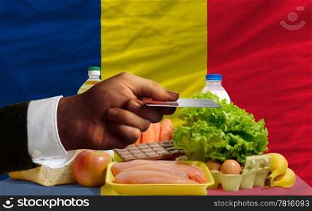 man stretching out credit card to buy food in front of complete wavy national flag of chad
