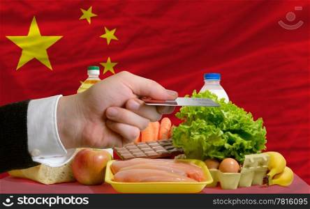 man stretching out credit card to buy food in front of complete wavy national flag of china