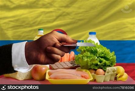 man stretching out credit card to buy food in front of complete wavy national flag of colombia
