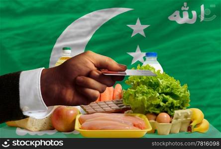 man stretching out credit card to buy food in front of complete wavy national flag of comoros