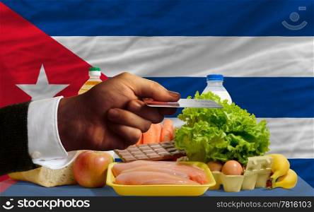 man stretching out credit card to buy food in front of complete wavy national flag of cuba