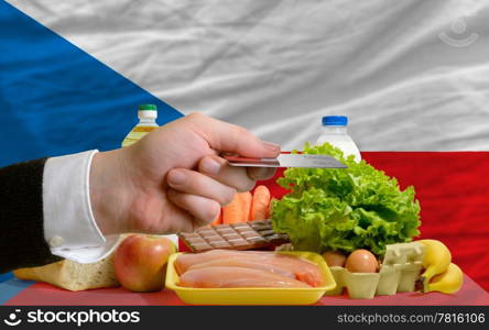 man stretching out credit card to buy food in front of complete wavy national flag of czech