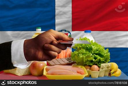 man stretching out credit card to buy food in front of complete wavy national flag of dominican