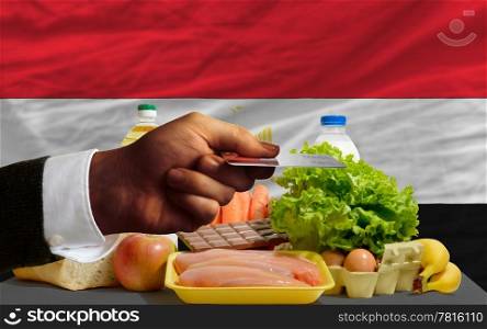 man stretching out credit card to buy food in front of complete wavy national flag of egypt