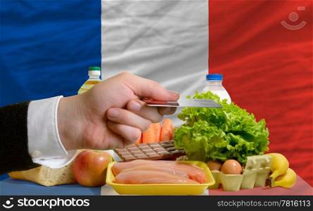 man stretching out credit card to buy food in front of complete wavy national flag of france
