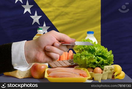 man stretching out credit card to buy food in front of complete wavy national flag of bosnia herzegovina