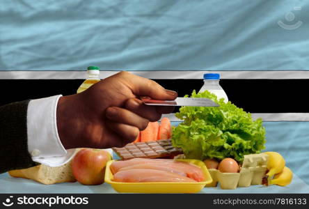 man stretching out credit card to buy food in front of complete wavy national flag of botswana