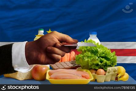 man stretching out credit card to buy food in front of complete wavy national flag of capeverde