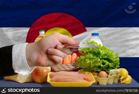 man stretching out credit card to buy food in front of complete wavy american state flag of colorado