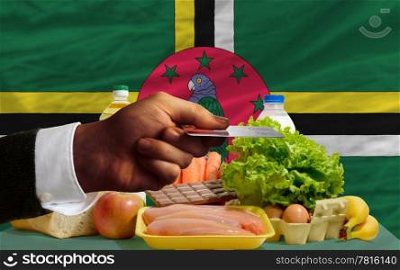 man stretching out credit card to buy food in front of complete wavy national flag of dominica