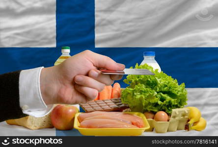 man stretching out credit card to buy food in front of complete wavy national flag of finland