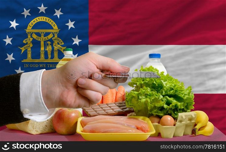 man stretching out credit card to buy food in front of complete wavy american state flag of georgia