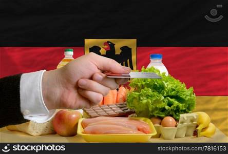 man stretching out credit card to buy food in front of complete wavy national flag of germany