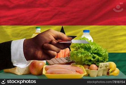 man stretching out credit card to buy food in front of complete wavy national flag of ghana