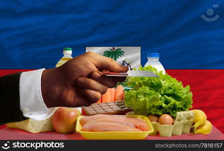 man stretching out credit card to buy food in front of complete wavy national flag of haiti