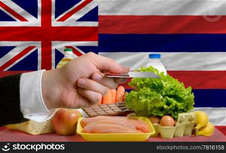 man stretching out credit card to buy food in front of complete wavy american state flag of hawaii