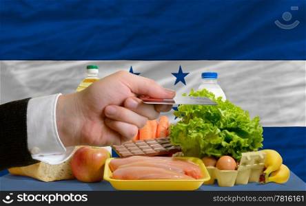 man stretching out credit card to buy food in front of complete wavy national flag of honduras