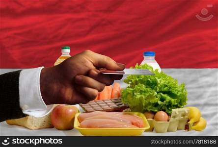 man stretching out credit card to buy food in front of complete wavy national flag of indonesia